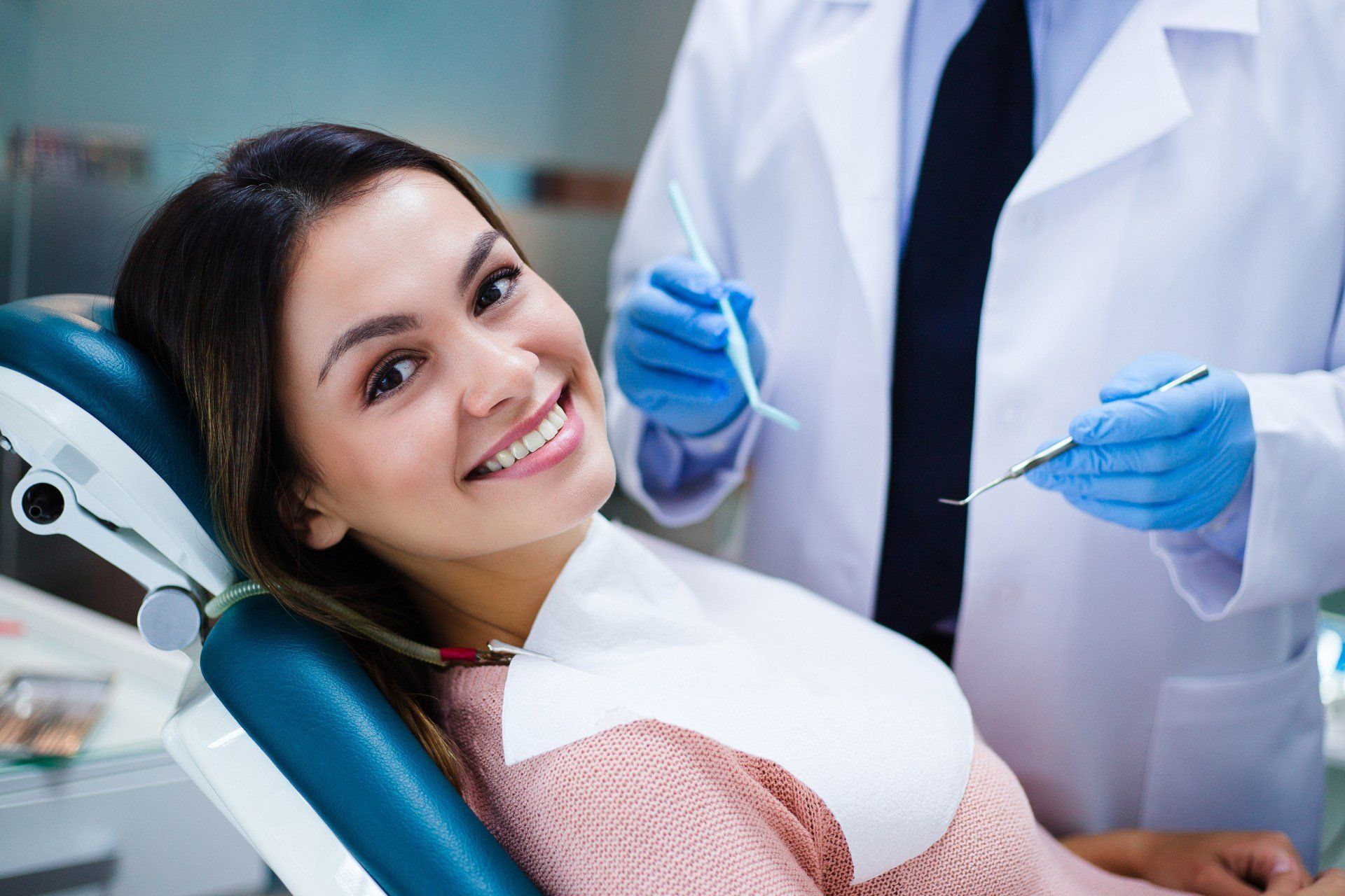 Paziente sorridente sulla poltrona odontoiatrica, accanto all'odontoiatra con gli strumenti in mano